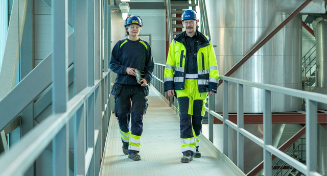 Two workers walking down a hallway in an industrial building.