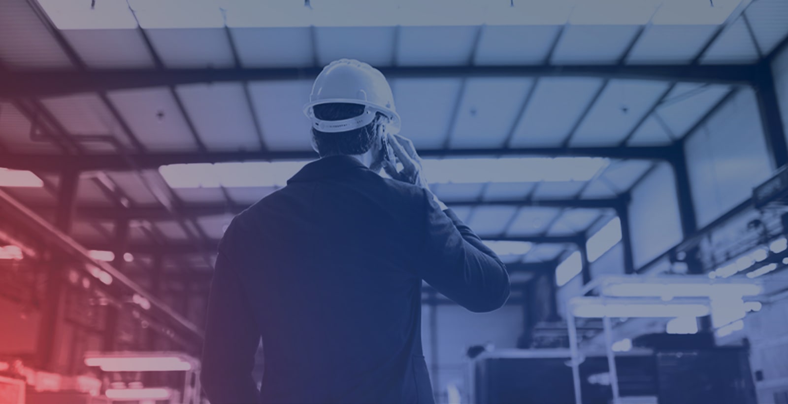 An operator stands on the plant floor with a cell phone up to his ear